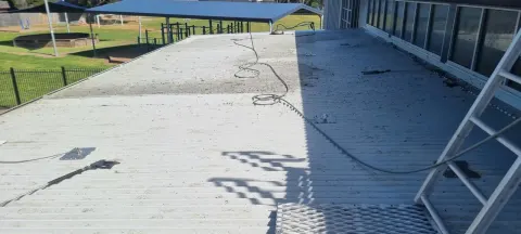 Commercial metal roof part-way through a high-pressure clean, with roof-safety anchor lines in place