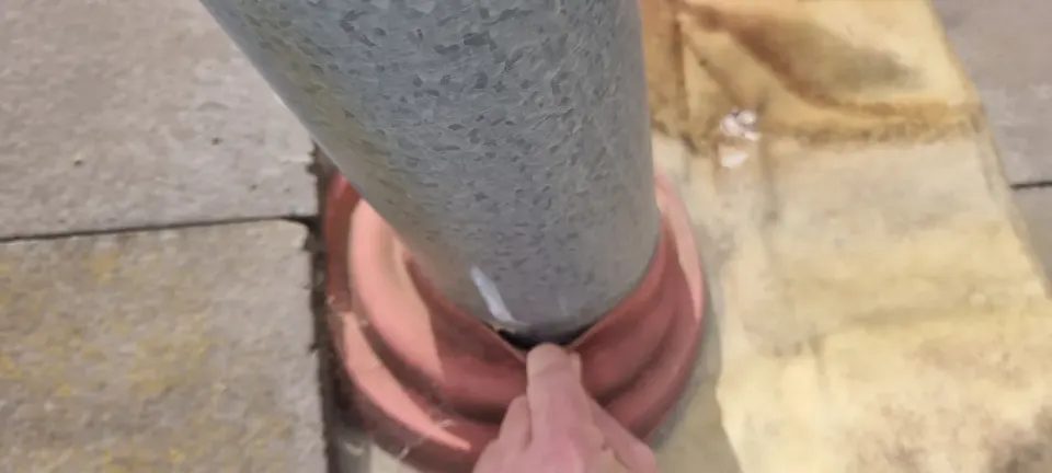 A finger pointing to a split in the flashing boot where a flue passes through a tiled roof